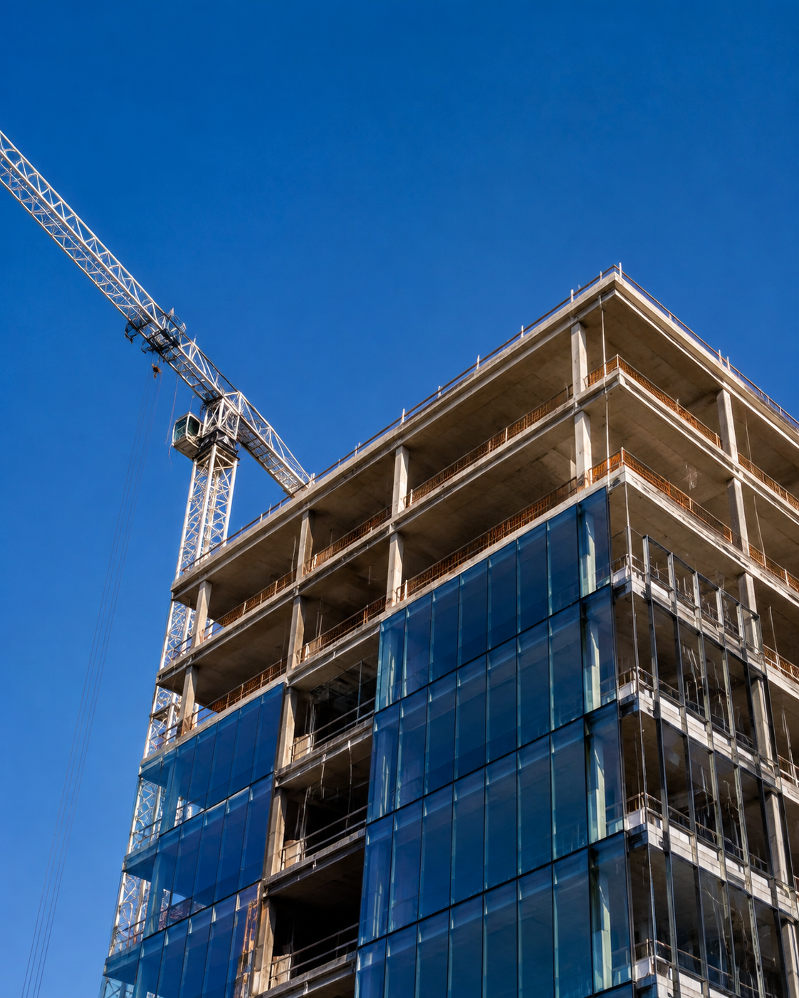 Concrete structure and blue glass facade of a building under construction beneath a tower crane
